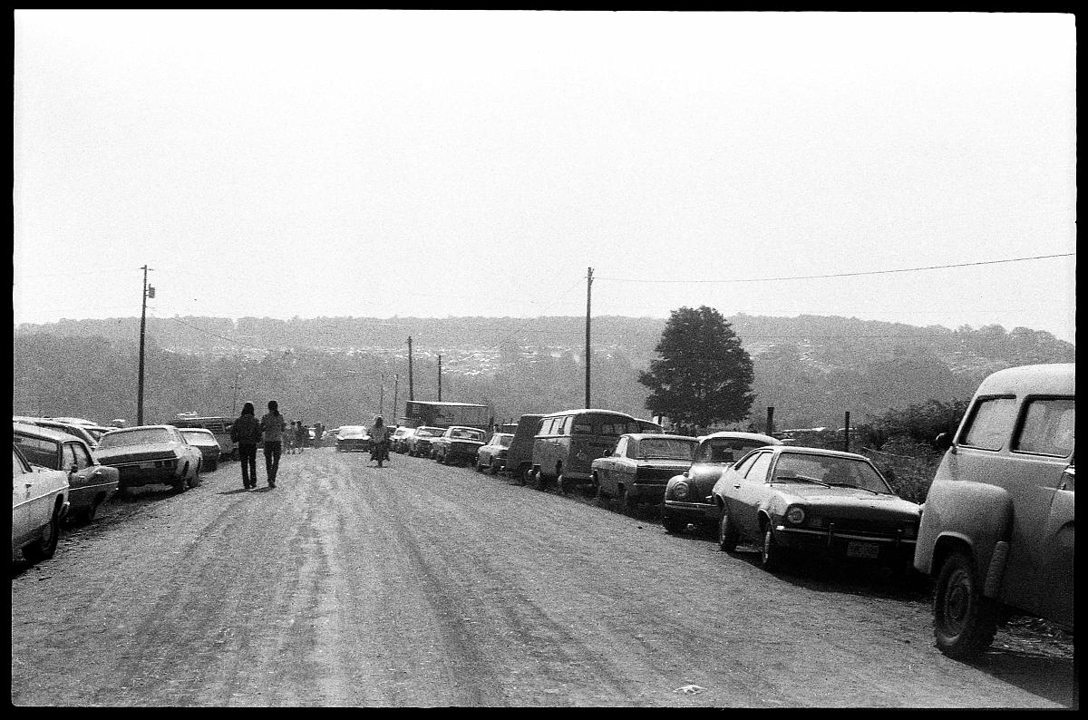 A03_055a.jpg -  Fortunately, we decided to drive out the day before the concert and camp out on the site.  Even so, we started seeing bumper-to-bumper traffic about twenty miles from the race track.  A lot of people just left their cars and walked.  A few of the roads, like this one, remained fairly clear thanks to the local and state police who were used to dealing with annual crowds of 100,000+ for the Grand Prix.   For the most part though, it was a mixture of creeping cars and strolling pedestrians.  When the cars did start moving, the walkers would all pile on the hoods and trunks and hitch a ride... when the line of cars stopped, they'd all hop off and start walking again.  Neither group made good time tho... the only ones who got thru quickly were those on bicycles and motorcycles.  It took us about two hours to cover the five miles from the center of town to the race track.